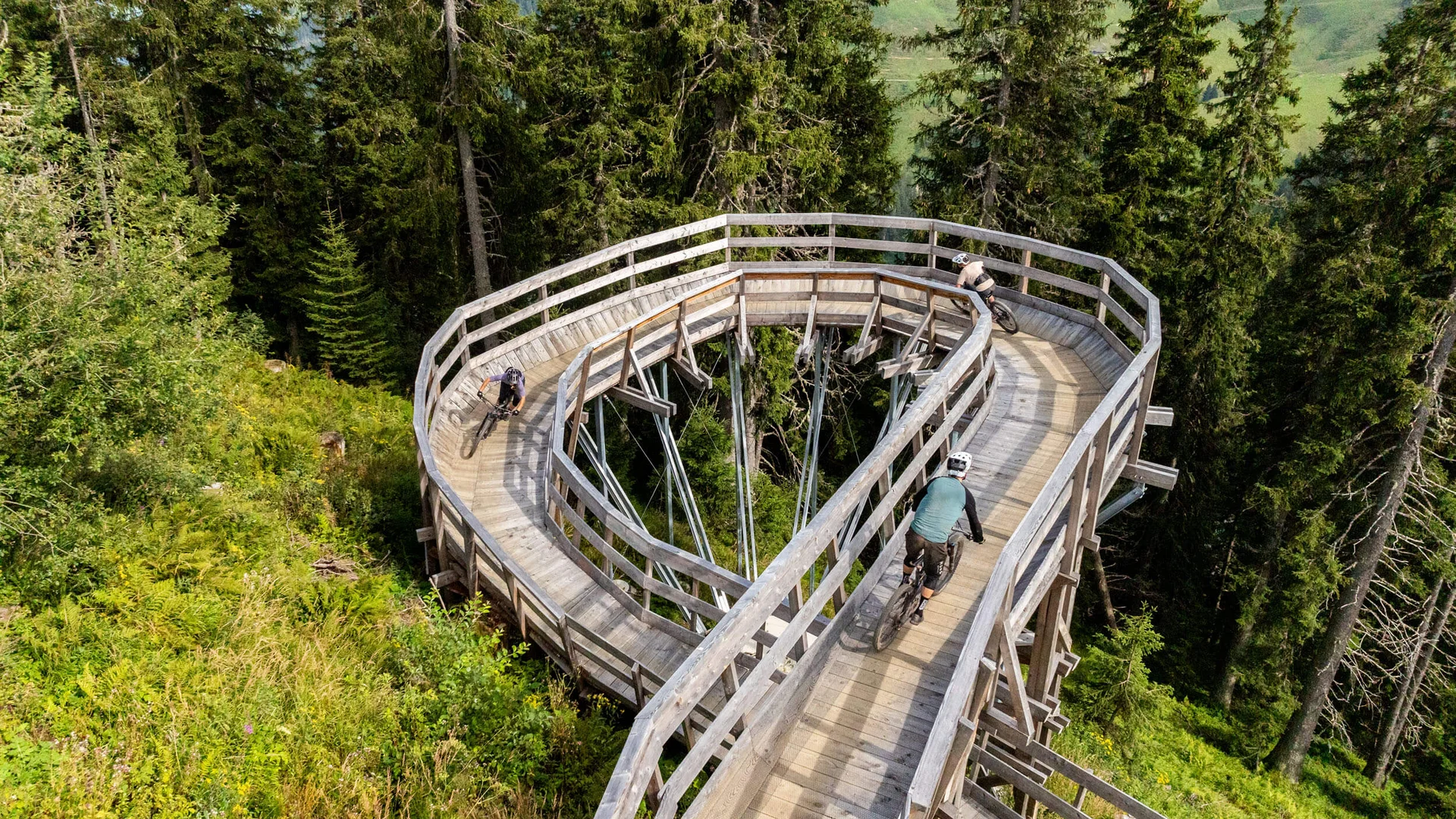 Neuer Flow im Brixental: Der Kirchberg Trail eröffnet © ZOOOMProductions Drei Mountainbiker fahren eine hölzerne Spirale im Wald hinunter