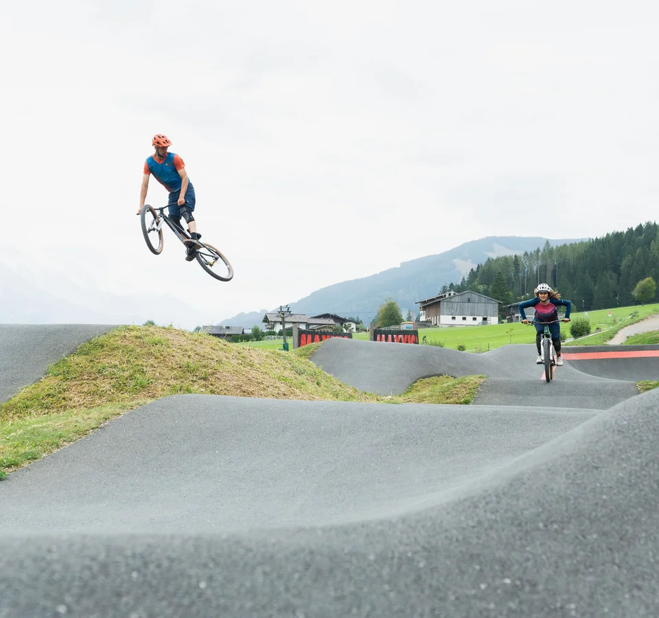 Twee fietsers maken sprongen op een buitenshuis BMX-pumptrack