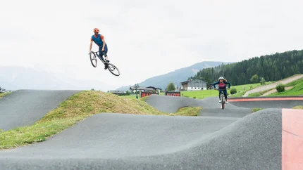 Zwei Fahrradfahrer üben Sprünge auf einem BMX-Pumptrack im Freien