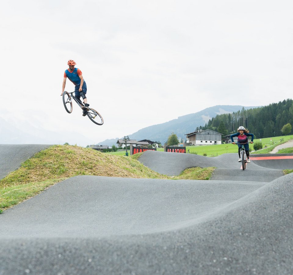 Two cyclists performing jumps on an outdoor BMX pump track
