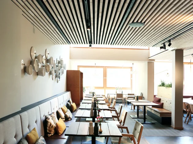 Best of Brandnertal © Klaus Andorfer Modernes Restaurant mit Holztischen, Stühlen und Wanddekoration aus weißen Schalen