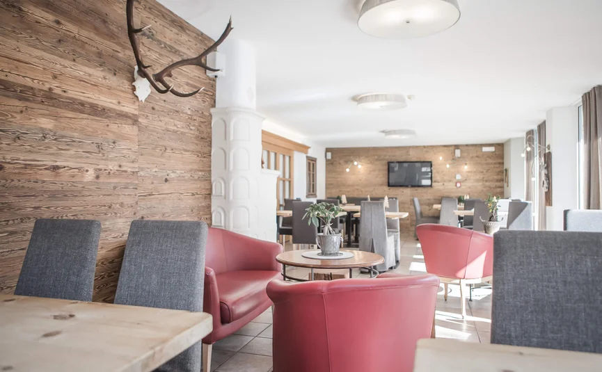 Bright restaurant with wooden decor, red armchairs, and gray chairs