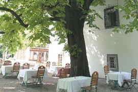 Week- Half-board Outdoor terrace with tables and chairs under trees next to white building