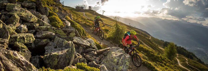 Zwei Mountainbiker fahren auf einem Bergpfad bei Sonnenuntergang