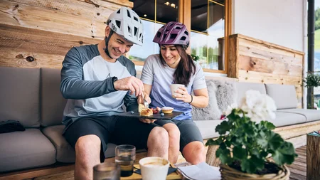 Ein perfekter Enduro-Tag – vom ersten Höhenmeter bis zum letzten Trail © Tobias Köhler Paar mit Fahrradhelmen teilt Kuchen und Kaffee auf einer Terrasse