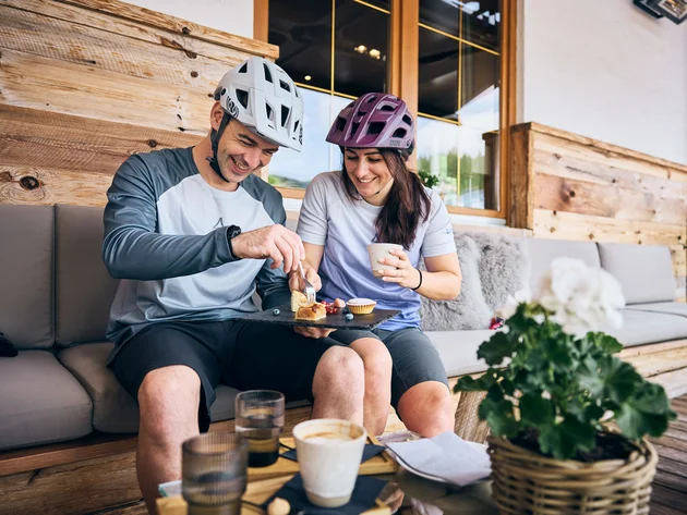 Ein perfekter Enduro-Tag – vom ersten Höhenmeter bis zum letzten Trail © Tobias Köhler Paar mit Fahrradhelmen teilt Kuchen und Kaffee auf einer Terrasse