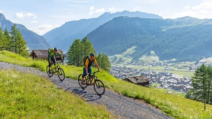 Zwei Mountainbiker fahren auf einem Bergweg mit Berglandschaft im Hintergrund