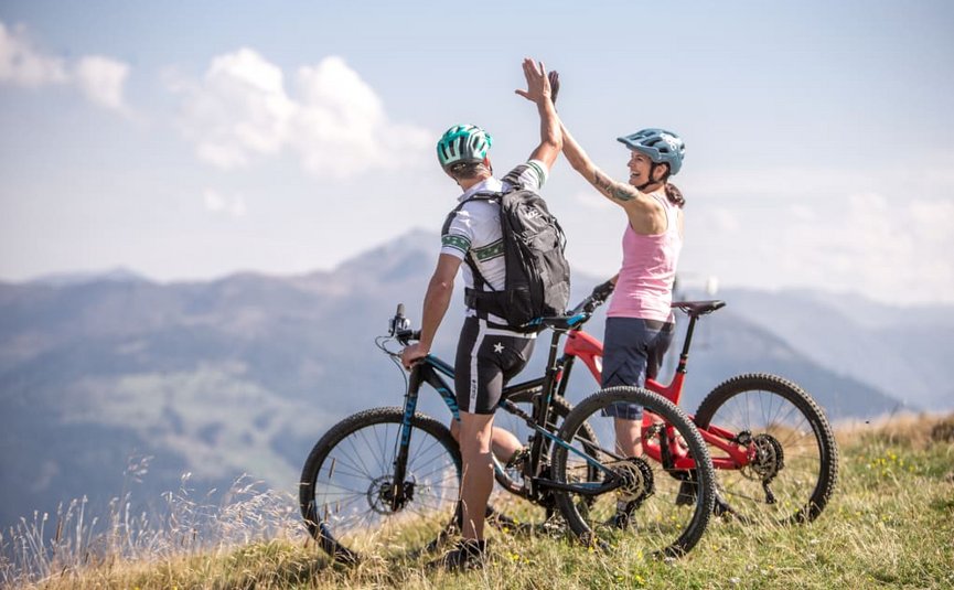 Bike week Two mountain bikers high five on a grassy hill with mountain view
