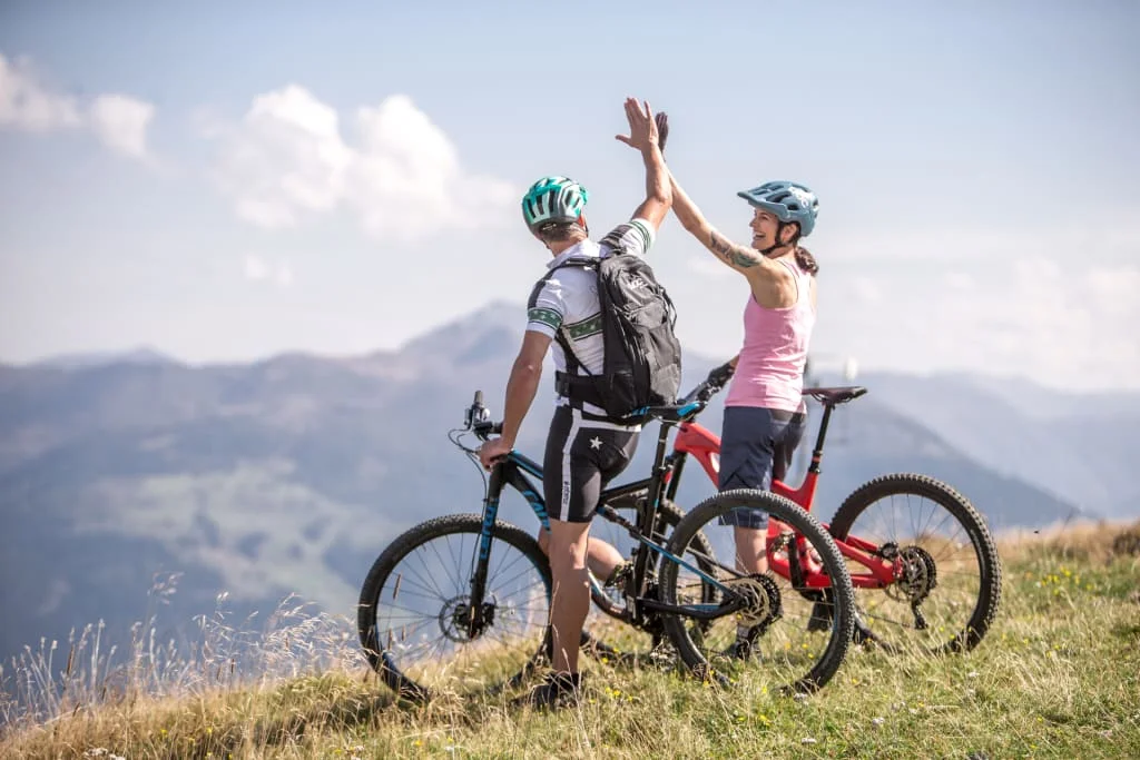 Twee mountainbikers geven elkaar high five op een grasheuvel met bergzicht