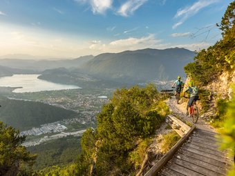 Zwei Mountainbiker fahren auf einem Bergpfad mit Blick auf Tal und See