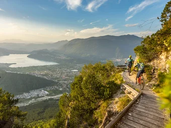 Two mountain bikers ride a trail overlooking a valley and lake