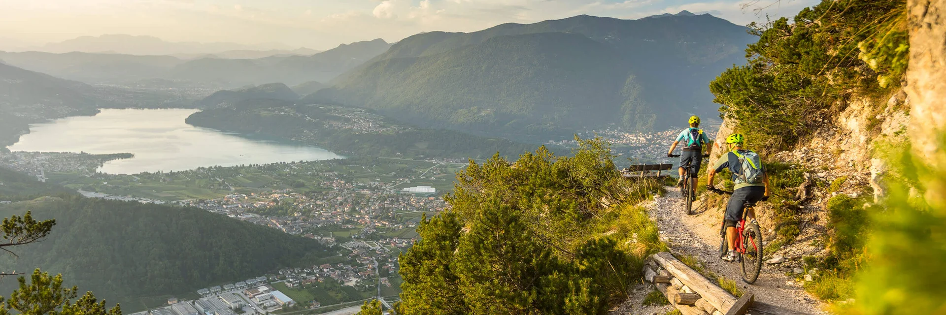 Two mountain bikers ride a trail overlooking a valley and lake
