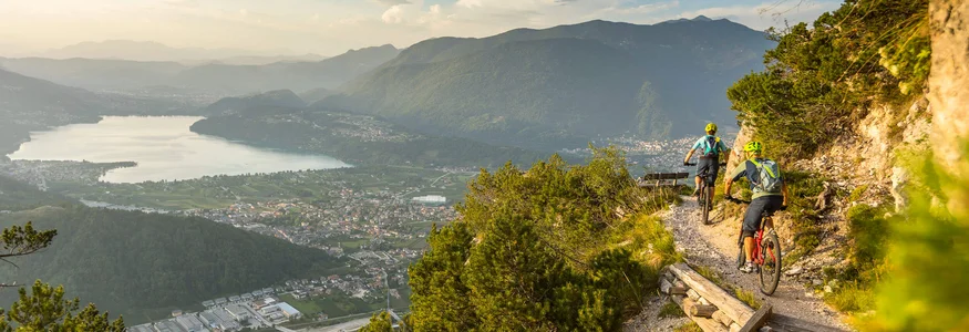 Two mountain bikers ride a trail overlooking a valley and lake