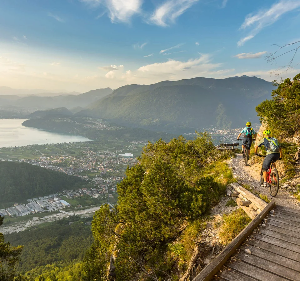 Zwei Mountainbiker fahren auf einem Bergpfad mit Blick auf Tal und See
