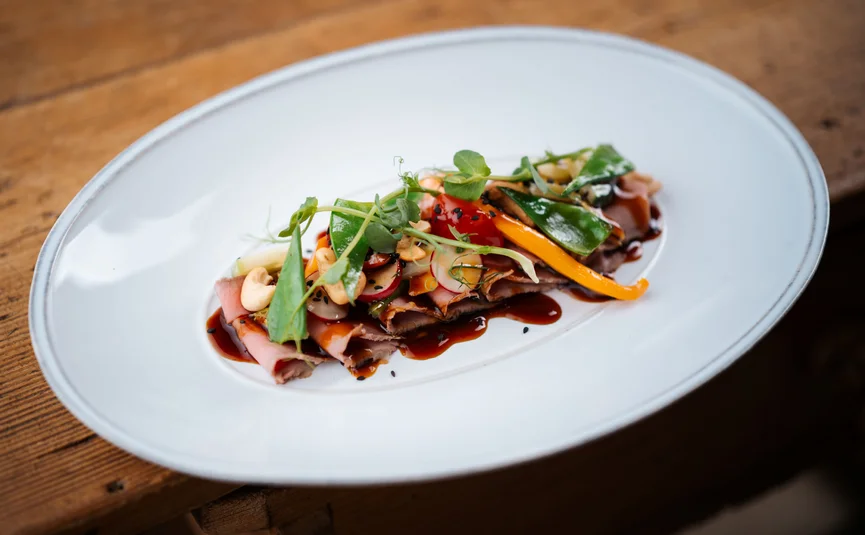 Fein angerichtetes Gericht mit Fleisch, Gemüse und Sauce auf weißem Teller