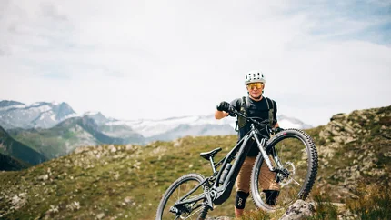 Mountainbiker mit Helm steht auf Felsen in bergiger Landschaft