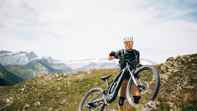 Mountainbiker mit Helm steht auf Felsen in bergiger Landschaft