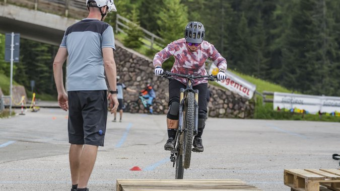 Fahrradfahrer springt über Holzpalette bei Mountainbike-Training mit Trainer