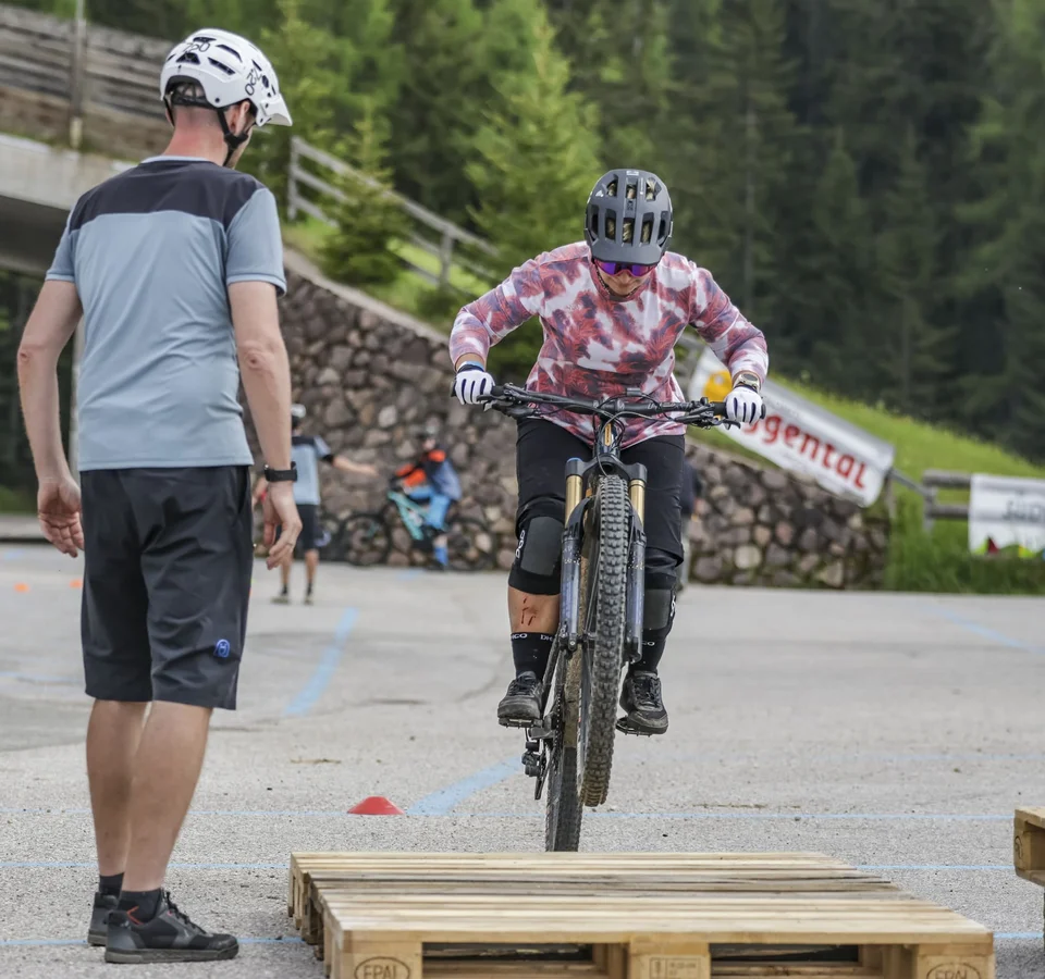 Fahrradfahrer springt über Holzpalette bei Mountainbike-Training mit Trainer