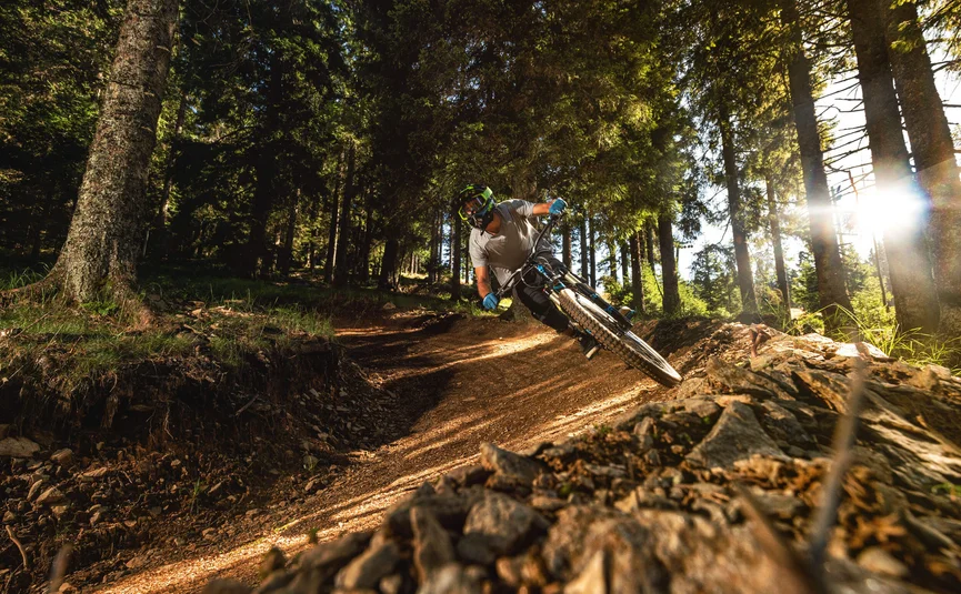 Mountainbiker rijdt op zonnig bospad met scherpe bocht