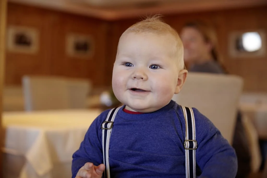Lachende baby met blauwe ogen en bretels binnen