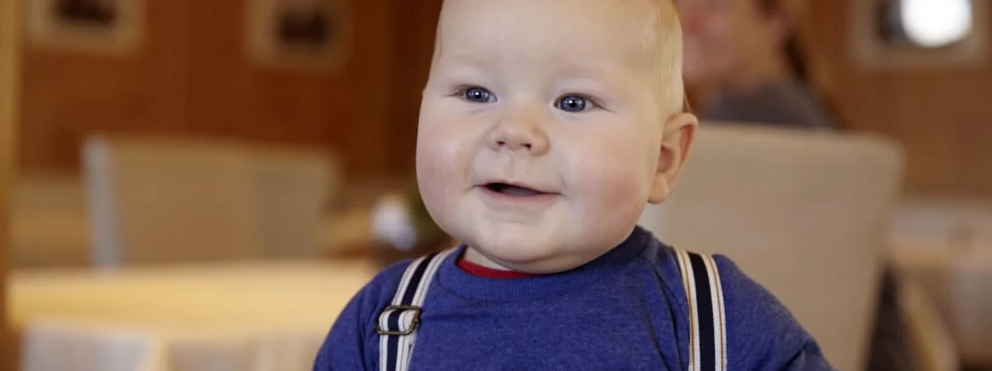 Lachende baby met blauwe ogen en bretels binnen