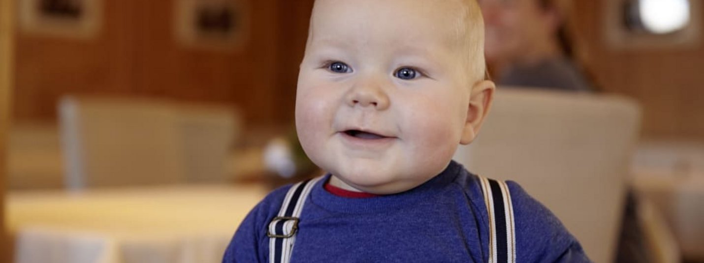 Lachende baby met blauwe ogen en bretels binnen
