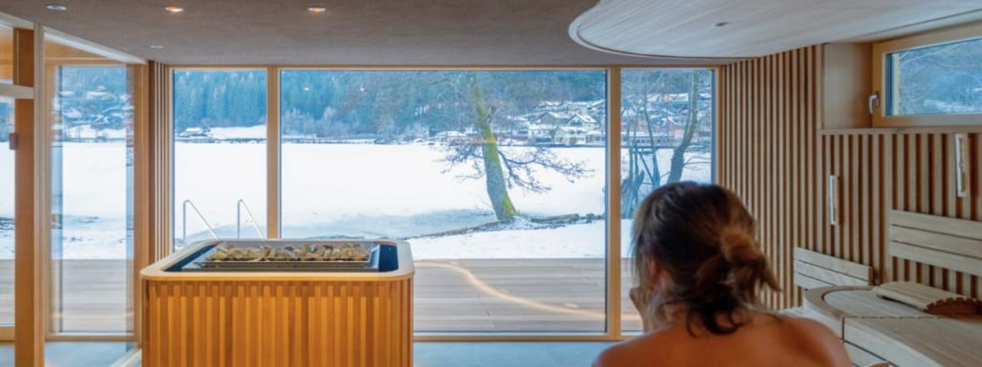 Brennseehof Saunatage Frau genießt Sauna mit Blick auf verschneite Landschaft durch große Fenster