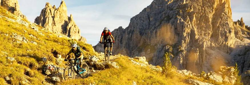 Two mountain bikers riding on a trail in a sunny mountain landscape