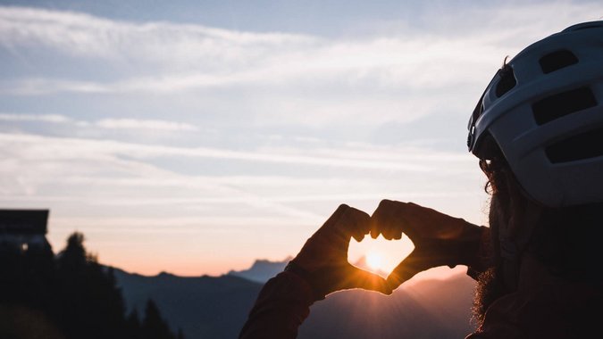 Fahrradfahrer formt Herz mit Händen vor dem Sonnenuntergang in den Bergen