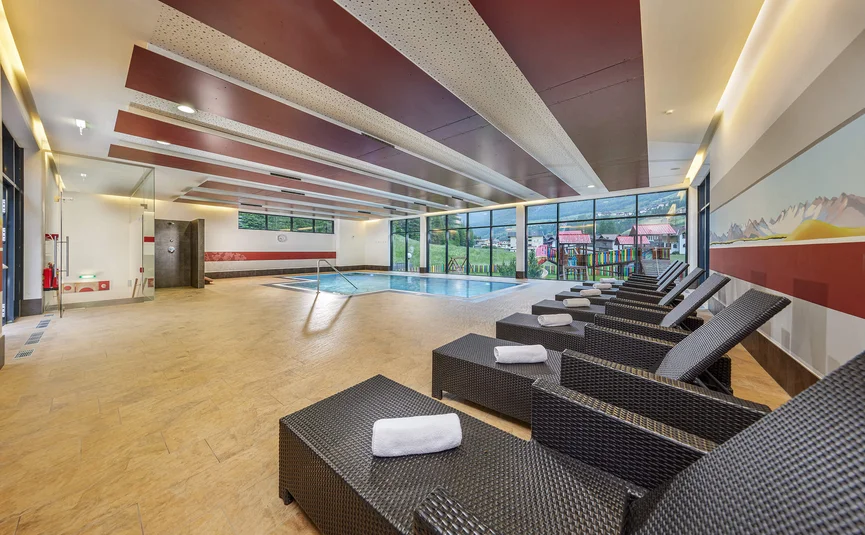 Indoor pool with lounge chairs and towels in a modern spa area
