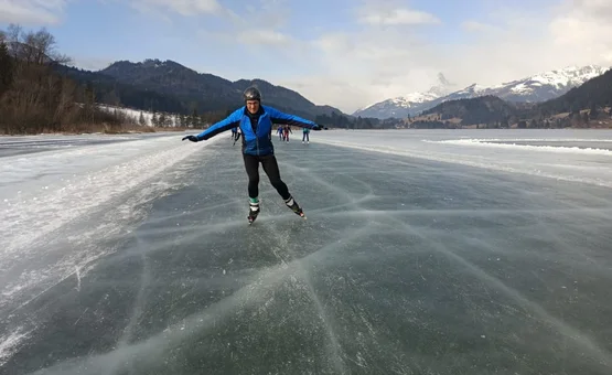 Person beim Eislaufen auf zugefrorenem See in den Bergen