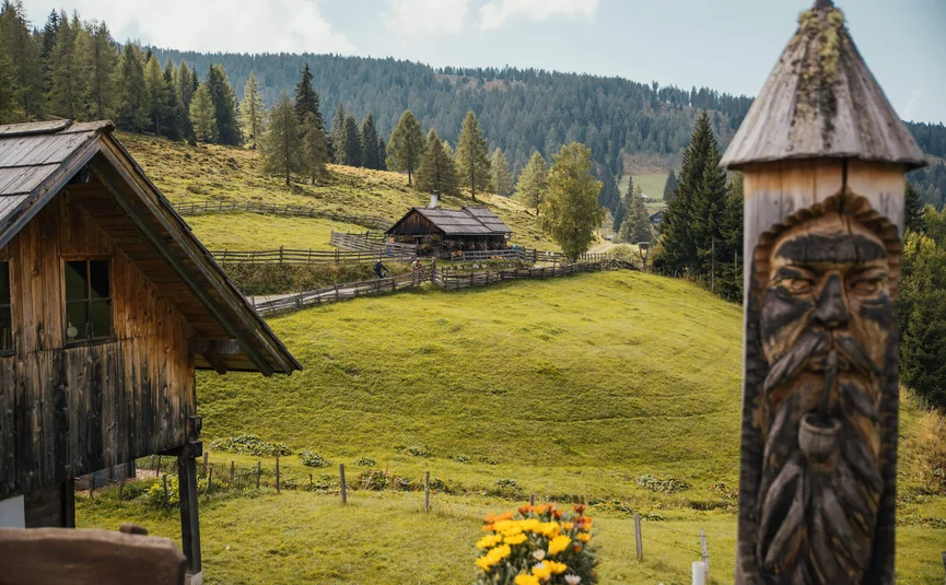 Almhütte mit geschnitztem Holzpfahl und grünen Hügeln im Hintergrund
