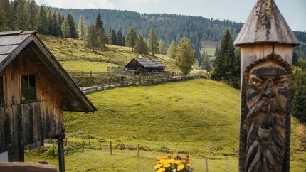 Almhütte mit geschnitztem Holzpfahl und grünen Hügeln im Hintergrund