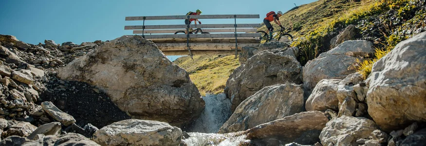 Zwei Mountainbiker fahren über eine Brücke über einen Bach in den Bergen