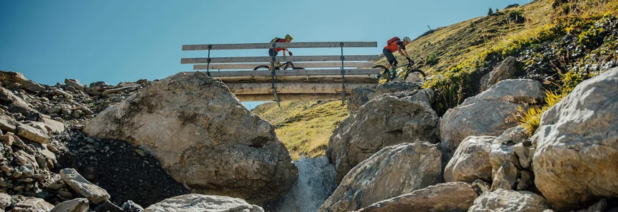 Zwei Mountainbiker fahren über eine Brücke über einen Bach in den Bergen