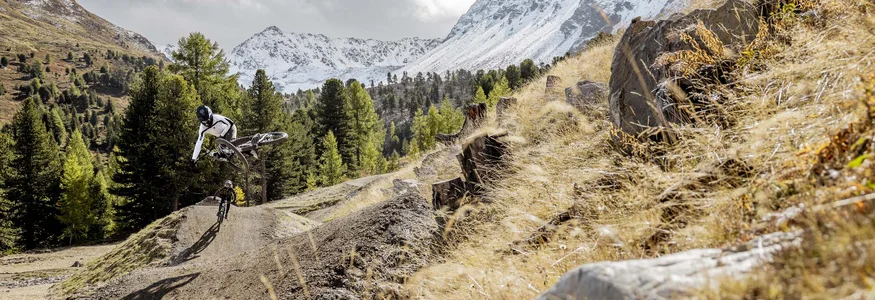 Mountainbiker springt auf einem Trail mit verschneiten Bergen im Hintergrund