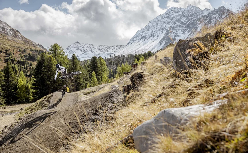 Mountainbiker springt auf einem Trail mit verschneiten Bergen im Hintergrund