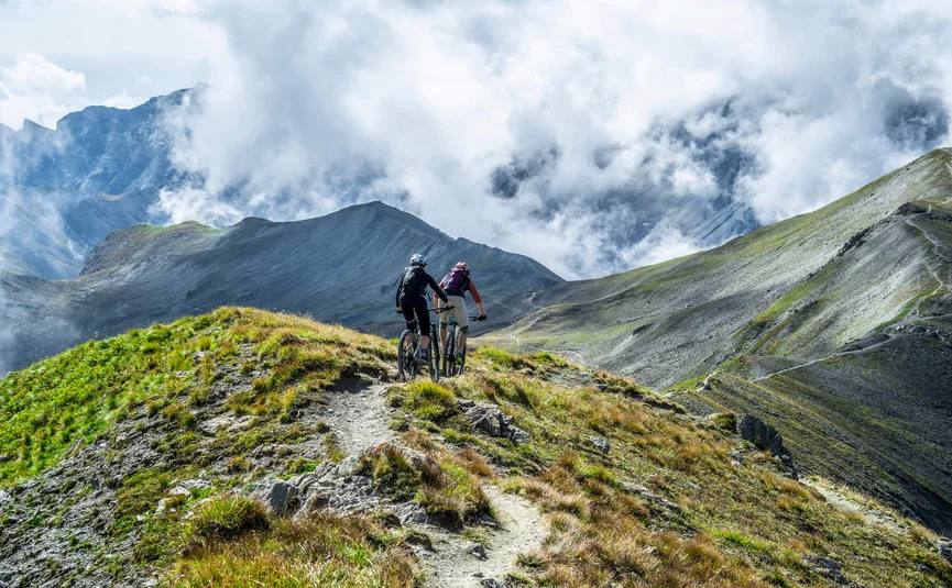 Two mountain bikers riding on a mountain trail with misty clouds