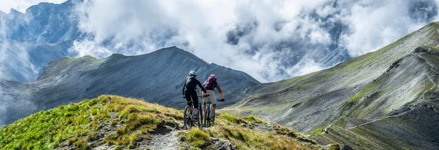Zwei Mountainbiker fahren auf einem Bergpfad mit Nebelschwaden