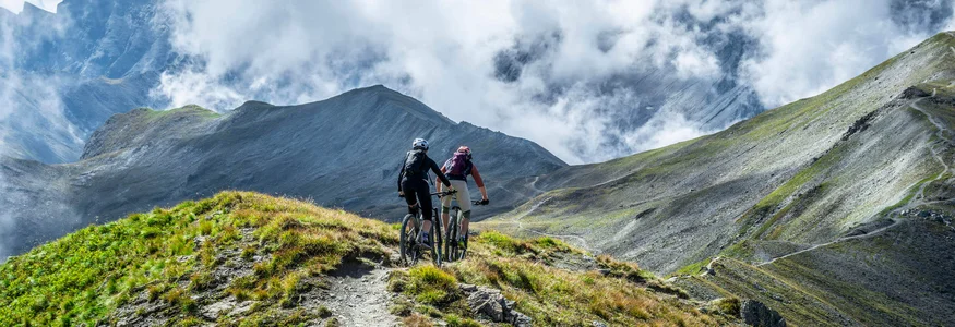 Zwei Mountainbiker fahren auf einem Bergpfad mit Nebelschwaden