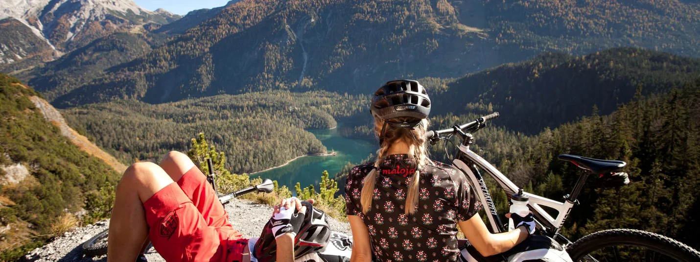 Two mountain bikers resting on bench overlooking mountains and lake