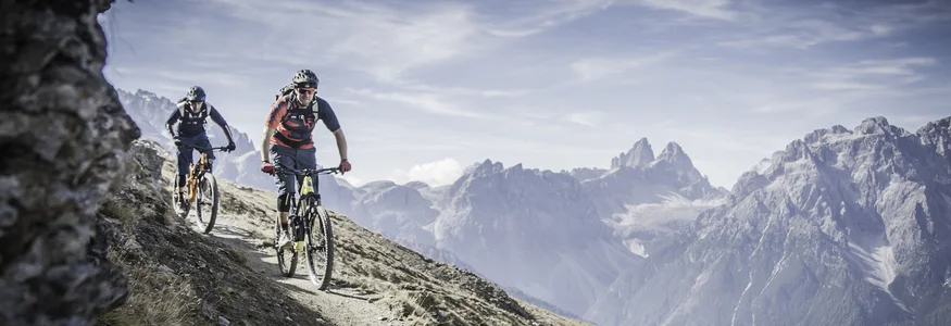 3 Zinnen Dolomites © Drei Zinnen Marketing - Manuel Kottersteger Zwei Mountainbiker fahren auf einem Bergpfad mit Alpen im Hintergrund