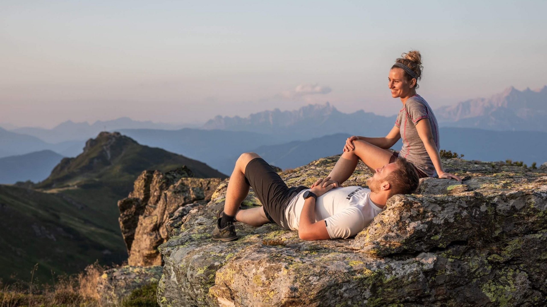 Paar entspannt auf Felsen mit Bergpanorama im Sonnenuntergang