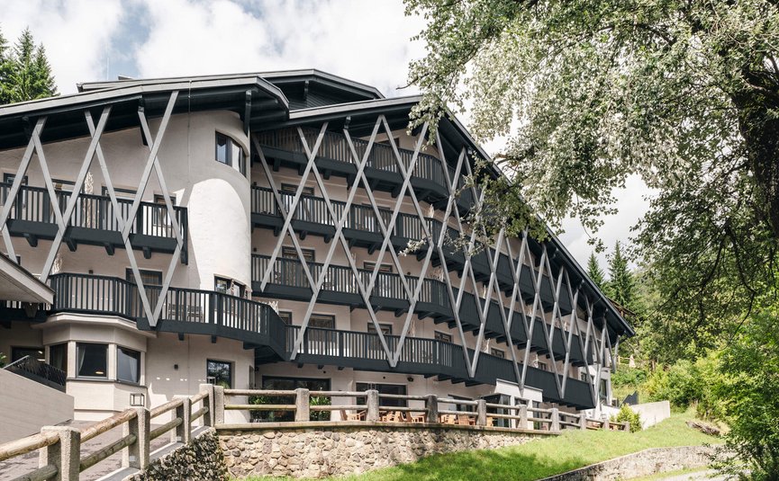 Hotel Arpuria | Hidden Luxury Mountain Home **** © Brandnamic Modernes mehrstöckiges Gebäude mit Balkonen und Holzgitterstruktur in grüner Landschaft