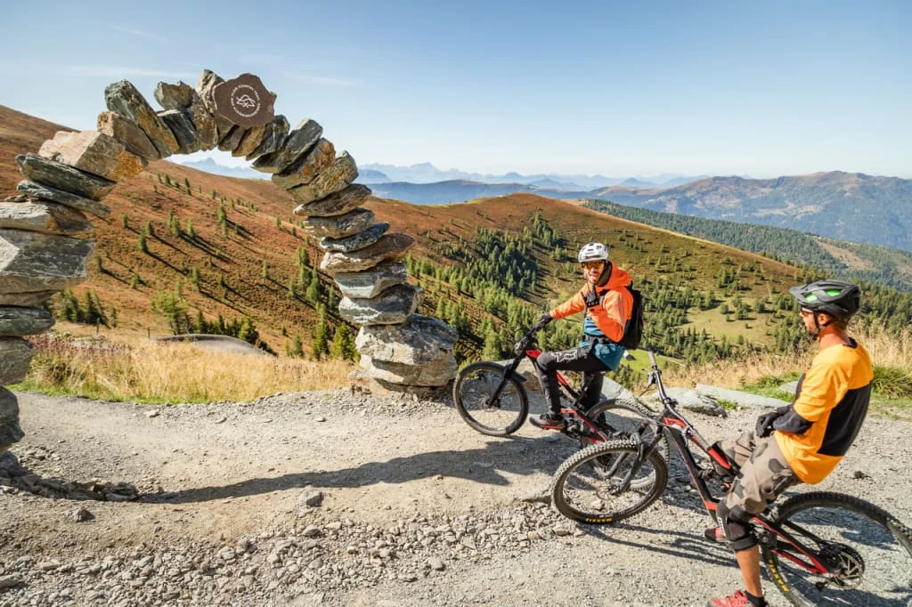 Two mountain bikers near a stone arch in the mountains on a clear day