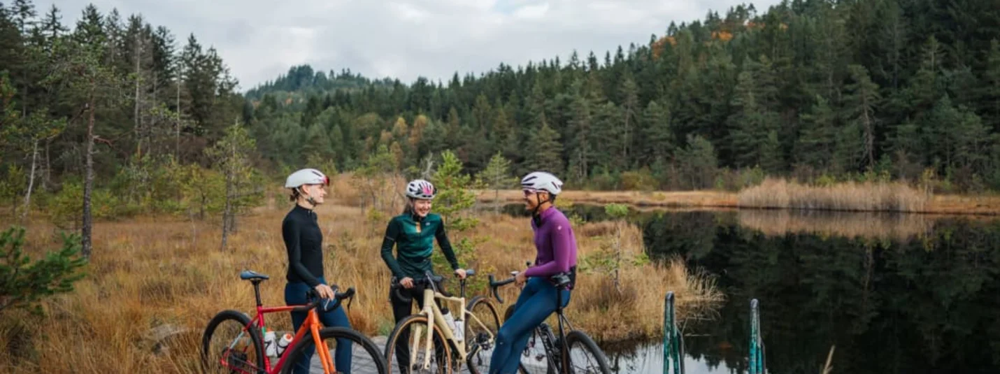 Three cyclists standing with bikes on a wooden pier by a lake in autumn forest