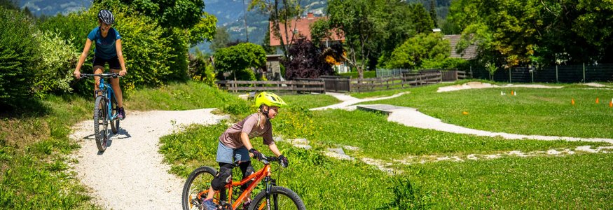 Kinder fahren Mountainbike auf einem sonnigen Waldweg in den Bergen