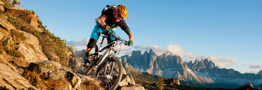 Mountainbiker fährt auf felsigem Bergpfad mit Alpen im Hintergrund