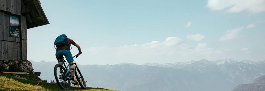 Bike und Hike – der alpine Trendsport, der das Beste aus zwei Welten vereint © David Karg Radfahrer auf Bergpfad neben Holzhütte mit Bergpanorama
